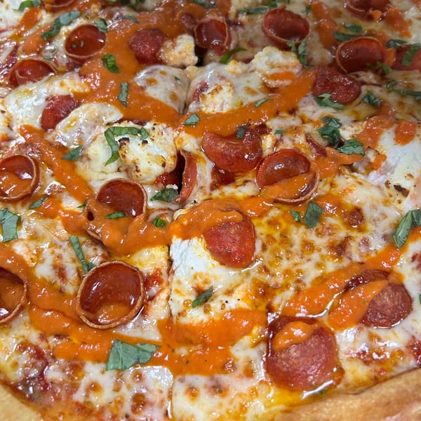 Close-up of a pepperoni pizza with melted cheese, dollops of ricotta, red sauce, and fresh basil.