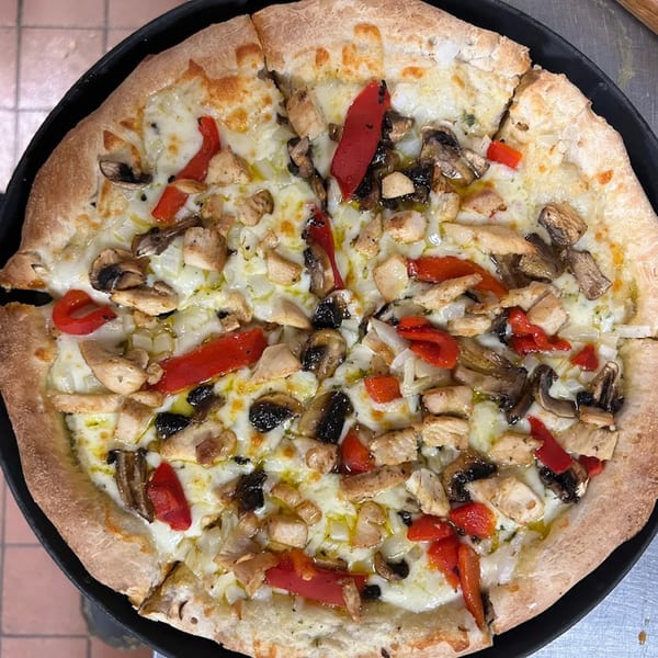 A freshly baked pizza with chicken, mushrooms, red peppers, and onions on a black pan.