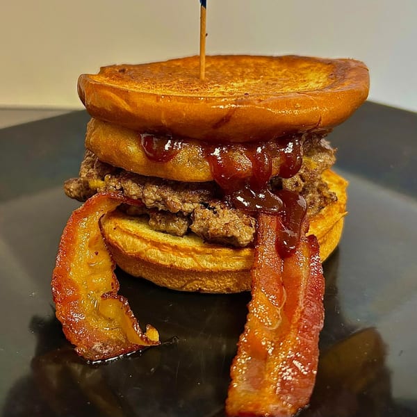 A tall burger with bacon, onion rings, and barbecue sauce on a toasted bun.