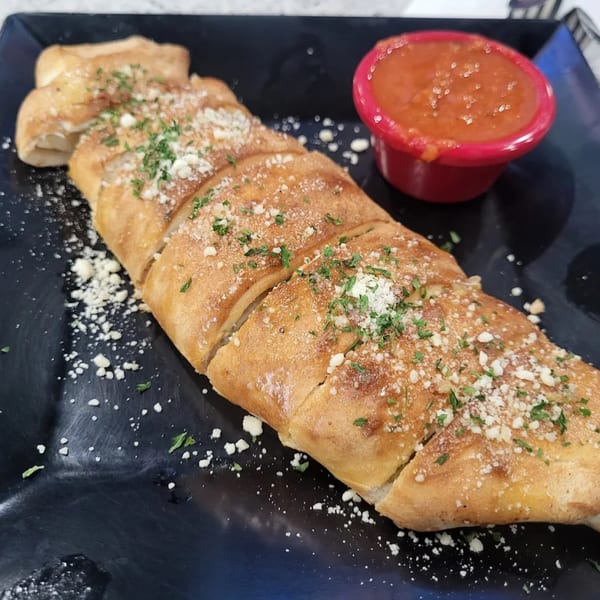 A golden-brown calzone, sliced and topped with parmesan and parsley, served with a side of marinara sauce.