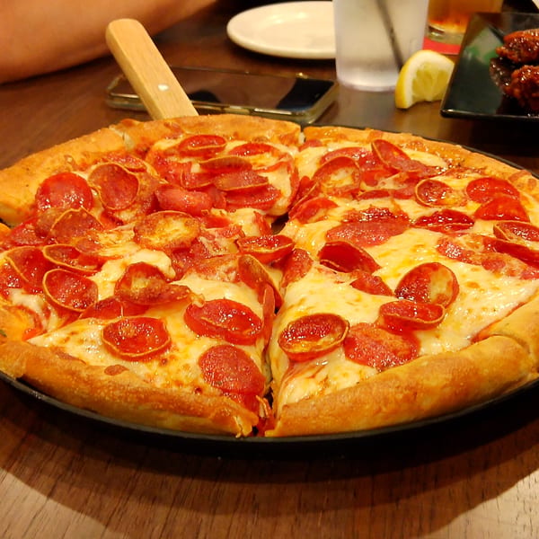 A large pepperoni pizza with melted cheese and a thick crust, served on a dark plate.